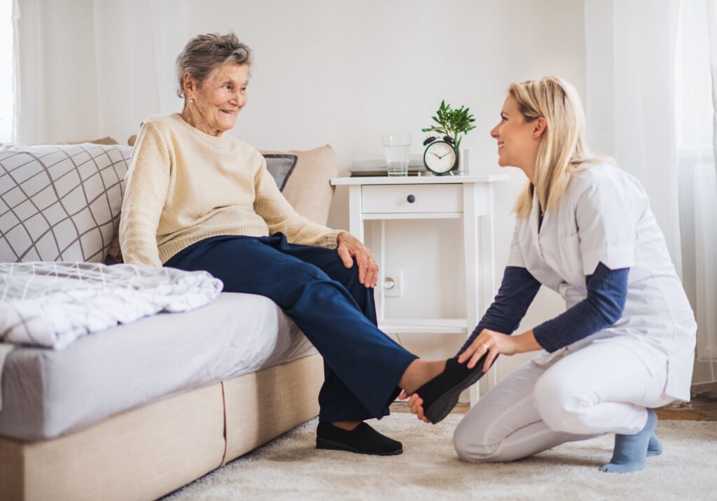 A health visitor putting on slippers on a senior woman at home at Christmas time.
