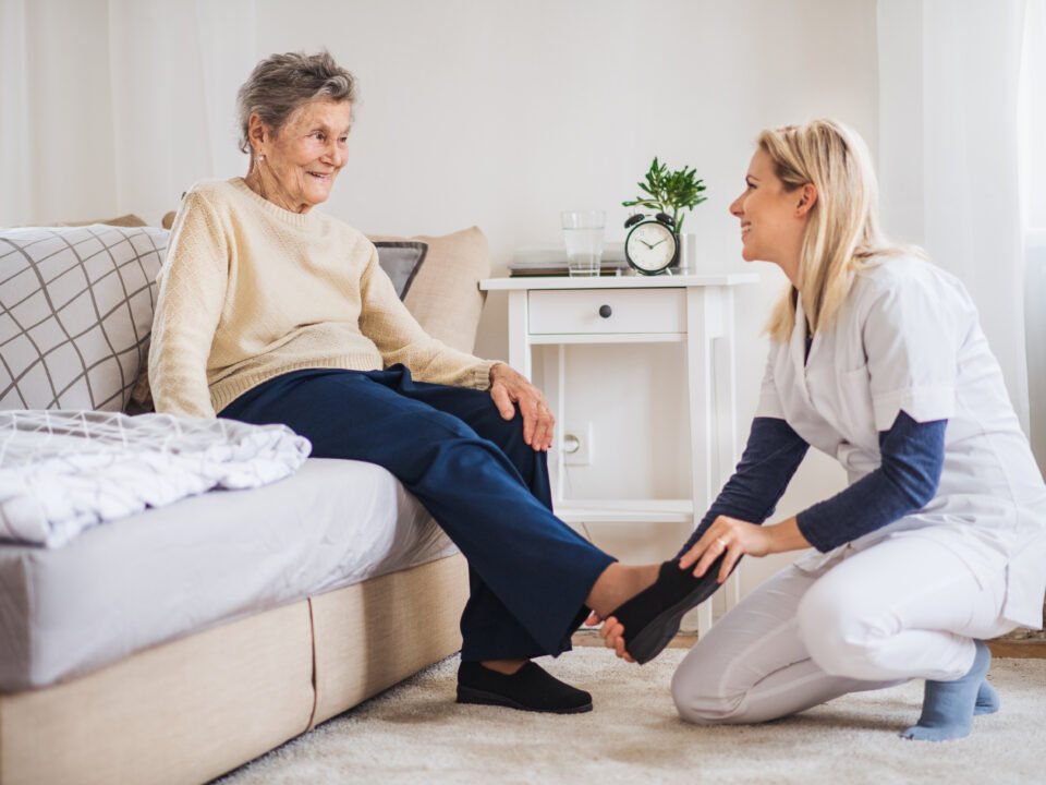 A health visitor putting on slippers on a senior woman at home at Christmas time.