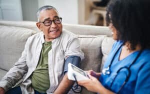 Shot of a senior man sitting with his nurse on the sofa while getting his blood pressure checked