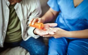 Cropped shot of an unrecognisable nurse sitting on the sofa with her senior patient and giving him pills